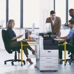 Teamarbeit in einem Büro mit bedruckten Papieren und dem Farb-Multifunktionsdrucker Xerox® VersaLink® C7100 Series